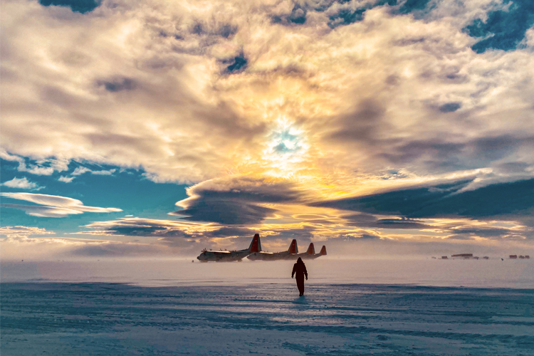 Edmond Tucker walking on snow with airplanes in background in Antartica